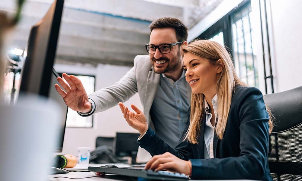 Employee Benefits for Small Businesses - Portrait of a Cheerful Business Man and Woman Looking at a Computer Together in the Office